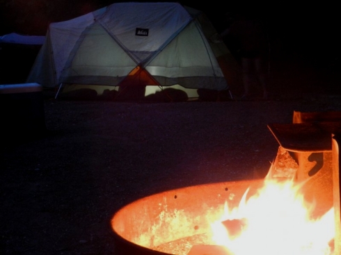 Photograph of a campfire with a tent in the background